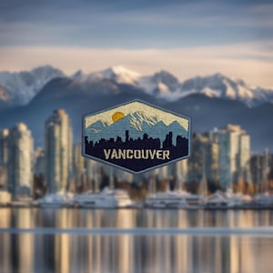 May include: A blue and white embroidered patch featuring a mountain range and a yellow sun. The text "VANCOUVER" is in white on a blue background.