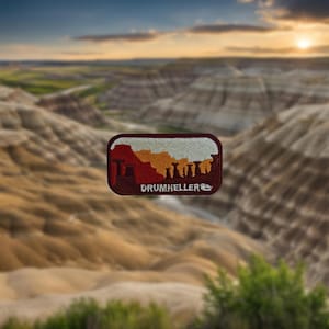May include: An embroidered patch in red, white and orange with the text "Drumheller" and a silhouette of a landscape with rock formations.