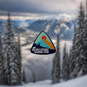 May include: A blue triangular patch with a mountain scene and a red sun. The text "Revelstoke National Park" is printed in white on the patch.