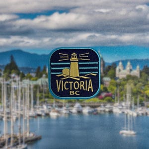 Puede incluir: Un parche bordado azul y dorado con un faro y el texto "VICTORIA BC".