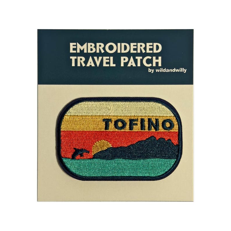 May include: Embroidered travel patch with a sunset scene and a dolphin jumping out of the water. The patch says "TOFINO" in black text.