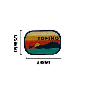 May include: A retro-style embroidered patch featuring a sunset over a mountain range with a dolphin jumping in the foreground. The patch is beige, red, orange, yellow, blue, and green with the word "TOFINO" in black text. The patch measures 3 inches wide and 1.75 inches tall.