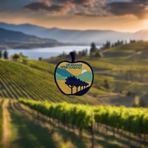 Peut inclure: Un patch brodé en forme de pomme avec le texte "OKANAGAN WINE COUNTRY" et une image stylisée d'un vignoble avec un soleil couchant derrière les collines.