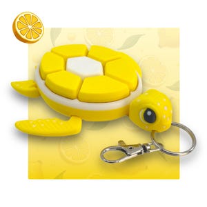 May include: A yellow turtle keyring with a segmented shell and a white underside. The turtle has a small, white face with black eyes and a silver key ring.