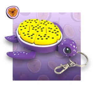 May include: A purple and yellow turtle keyring with a passion fruit design. The turtle has a white shell with black dots and a purple body with white dots. The keyring has a silver metal ring.
