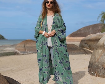 May include: A long, green and blue tie-dye kimono with a white undergarment. The kimono has a relaxed fit and is made of a lightweight fabric. The model is wearing white sandals.