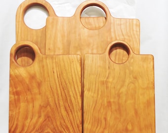 May include: Four rectangular wooden chopping boards with rounded top edges and circular handle cutouts. The boards feature a warm, light brown natural wood grain pattern with visible textures and smooth surfaces, arranged in a layered, overlapping stack.