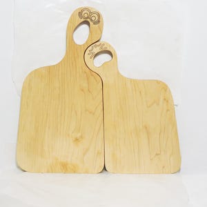 May include: Two wooden cutting boards with light wood grain. One board has a handle with an owl design, and the other has a handle with a paw print design. The boards are rectangular with rounded corners.