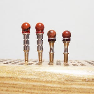 May include: Four decorative metal and stone game pieces with red and silver accents. The pieces are arranged in a row on a wooden surface.
