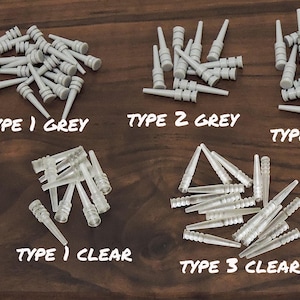 May include: An assortment of small, plastic components in gray and clear. The image is labeled with text indicating different types: Type 1 Grey, Type 2 Grey, Type 4 Grey, Type 1 Clear, and Type 3 Clear. The components are on a dark wood surface.