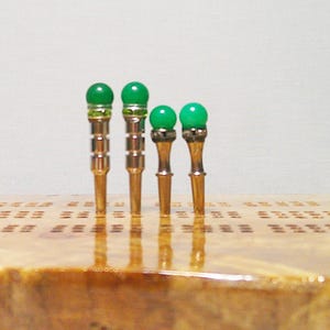 May include: Four silver and green decorative metal pins with rounded tops. The pins are arranged in order of size from largest to smallest.
