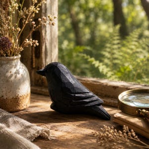 May include: A small, hand-carved black wooden bird figurine with visible chisel marks on its surface. The bird is positioned in profile, facing left, with a pointed beak and layered wing details, showcasing a matte finish and dark texture.