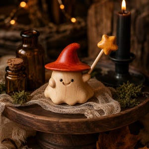 Peut inclure: Une petite figurine de fantôme en bois avec un corps clair et lisse, un visage sculpté souriant aux yeux noirs et un chapeau pointu rouge vif. Le fantôme tient une baguette en bois brun clair surmontée d'une étoile à cinq branches.