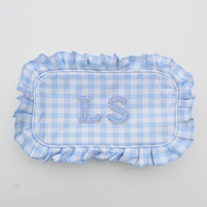 May include: A light blue and white gingham pattern pillow with a ruffled edge. The pillow features the embroidered initials "LS" in a decorative font, embellished with small, sparkling beads.