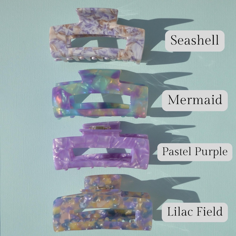 May include: Four colorful hair claw clips in Seashell, Mermaid, Pastel Purple, and Lilac Field patterns. Each clip has a rectangular shape with a curved top and a metal clasp. The background is a light blue.
