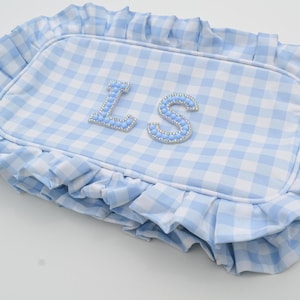 May include: A rectangular, light blue and white gingham patterned pillow with a ruffled edge. The pillow features the letters "LS" in a light blue, beaded font.