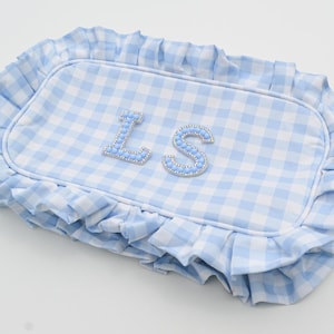 May include: A light blue and white gingham patterned pillow with a ruffled edge. The pillow features the letters "LS" in light blue with a beaded trim. The pillow is rectangular in shape.