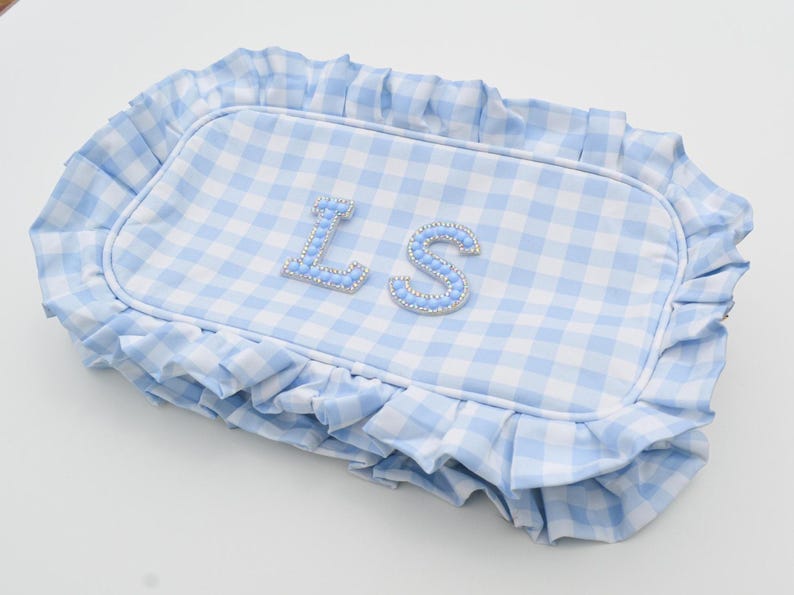 May include: A light blue and white gingham patterned pillow with a ruffled edge. The pillow features the letters "LS" in light blue with a beaded trim. The pillow is rectangular in shape.