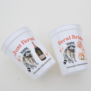 May include: Two white plastic cups with the phrases "Just Feral" and "Feral Bride" in red script. Each cup features a watercolor raccoon illustration and the text "Amanda's Bachelorette". One cup has a champagne bottle.