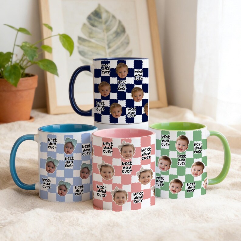 May include: Four ceramic mugs with the text "best dad ever" and baby faces on a checkered pattern. The mugs have blue, pink, green, and navy blue accents. The mugs are a standard size for coffee or tea.
