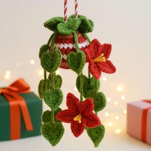 May include: Crocheted Christmas ornament featuring a red and white striped bell shape with green leaves and red flowers. The ornament is suspended by a red and white striped cord. The leaves are heart-shaped.
