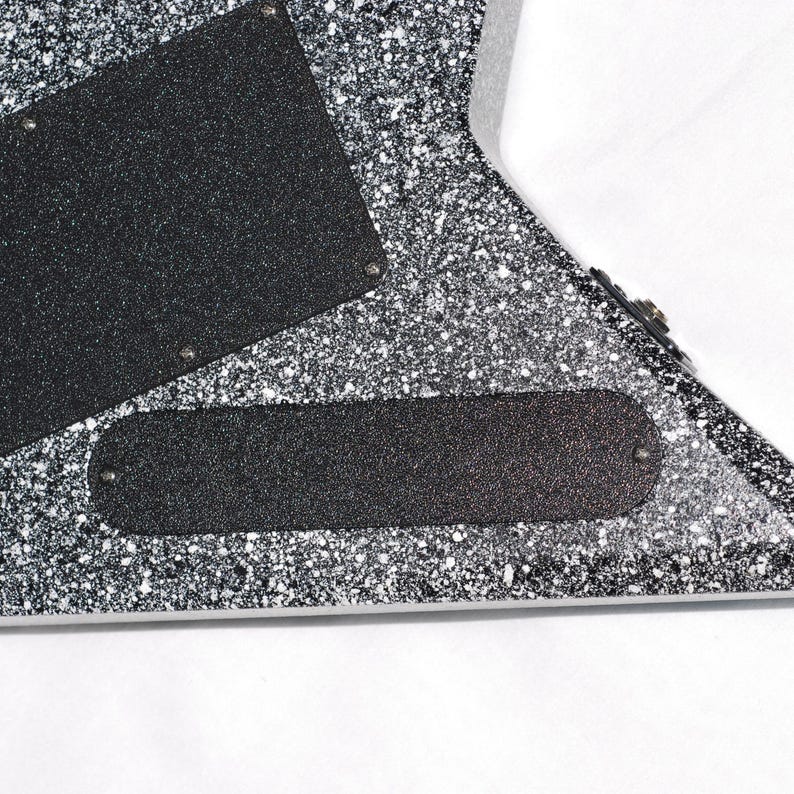 May include: Close-up of a guitar body with a speckled black and silver finish. The image shows two black textured plates and a black oval-shaped plate, all attached with small silver screws. The guitar's edge is visible.