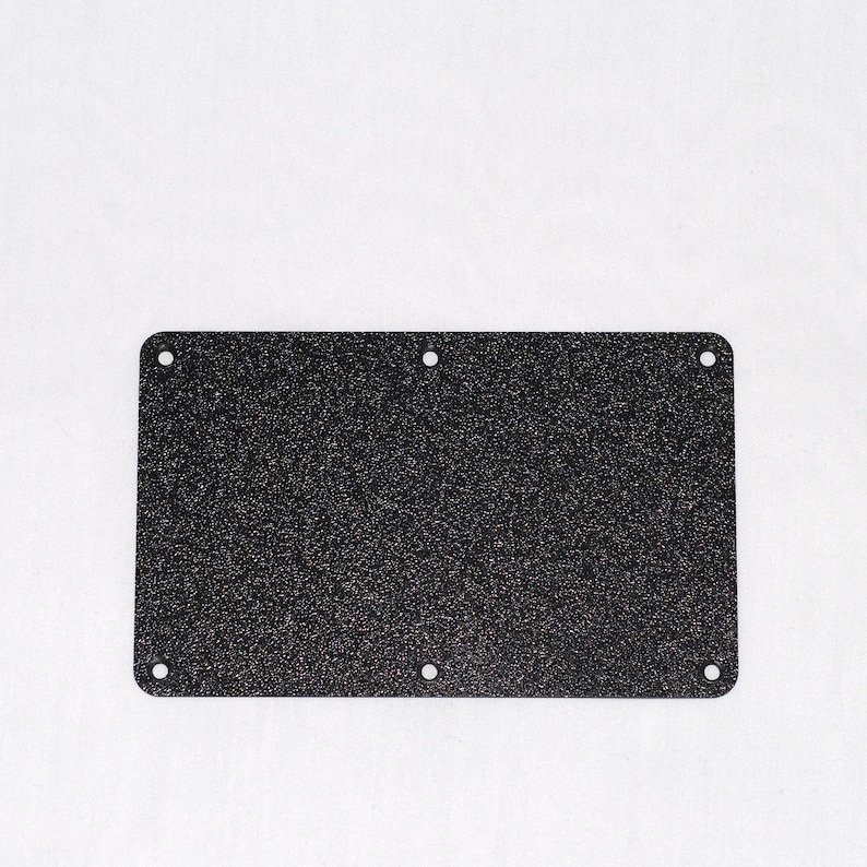 May include: A rectangular, dark speckled metal plate with rounded corners and six evenly spaced holes. The plate has a textured surface and is set against a white background.