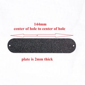 May include: A black, rectangular plate with rounded ends and a textured surface. The plate is 2mm thick and has two holes. The distance from the center of one hole to the other is 144mm.