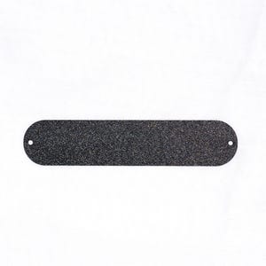 May include: A long, oval-shaped, black metal plate with a textured surface and rounded ends. Two small holes are drilled near the ends. The plate is set against a white background.