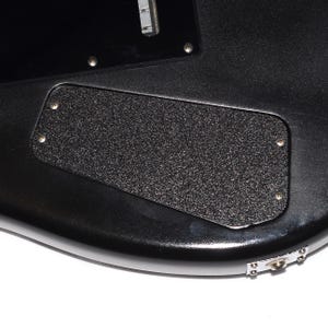 May include: Close-up of the back of a black electric guitar. The guitar features a textured, rectangular black plate secured with four screws. The body of the guitar is a glossy black, with a silver jack plate and a few visible screws.