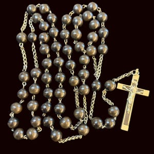 May include: A rosary with dark brown wooden beads and silver-colored chain links. The rosary features a gold-colored crucifix with a detailed depiction of Jesus Christ.