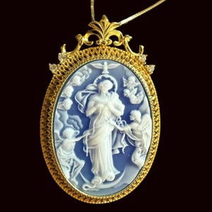 May include: Gold-tone pendant necklace featuring an oval cameo with a blue background and white relief carving of a religious figure, angels, and a dove. The pendant is framed with a detailed gold border and small diamonds, suspended from a delicate gold chain.