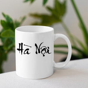 May include: White ceramic mug with a black design that says "Ha Noi" in a stylised font.
