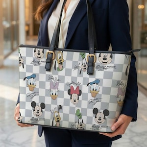 May include: A gray and white checkered tote bag featuring Disney characters like Mickey Mouse, Donald Duck, and Minnie Mouse. The bag has black handles and gold-colored buckles. The bag is held by a person wearing a navy blue blazer.
