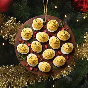 May include: A Christmas tree ornament resembling a wooden serving board, decorated with devilled eggs, cranberries, and bacon pieces. The ornament hangs from a gold string against a backdrop of a decorated Christmas tree with red baubles and gold tinsel.