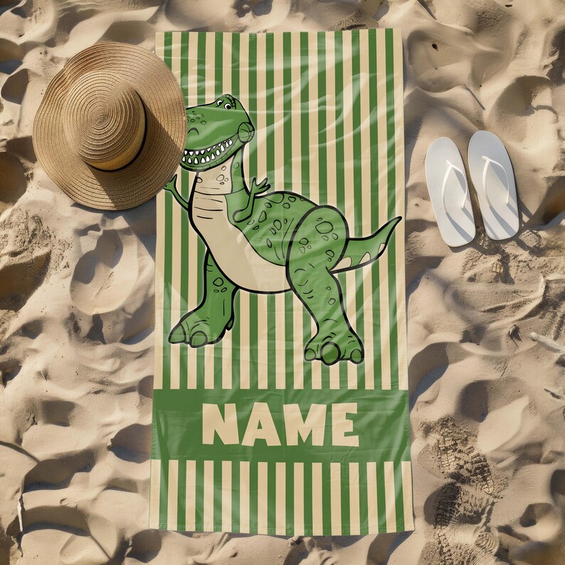 May include: Green and beige striped beach towel with a cartoon dinosaur illustration and the word "NAME" printed on it.