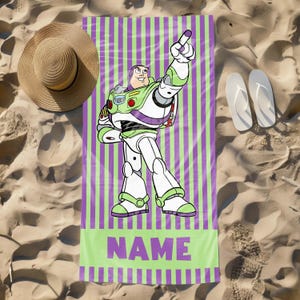 May include: A green and purple striped beach towel with a cartoon image of Buzz Lightyear from Toy Story. The towel has the word "NAME" printed in purple letters.