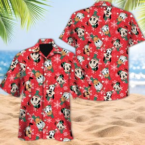 May include: Red short-sleeved button-down shirt with a repeating pattern of Mickey Mouse, Donald Duck, Goofy, and snowflakes. The characters wear Santa hats on a red background. The shirt is displayed on a sandy beach.