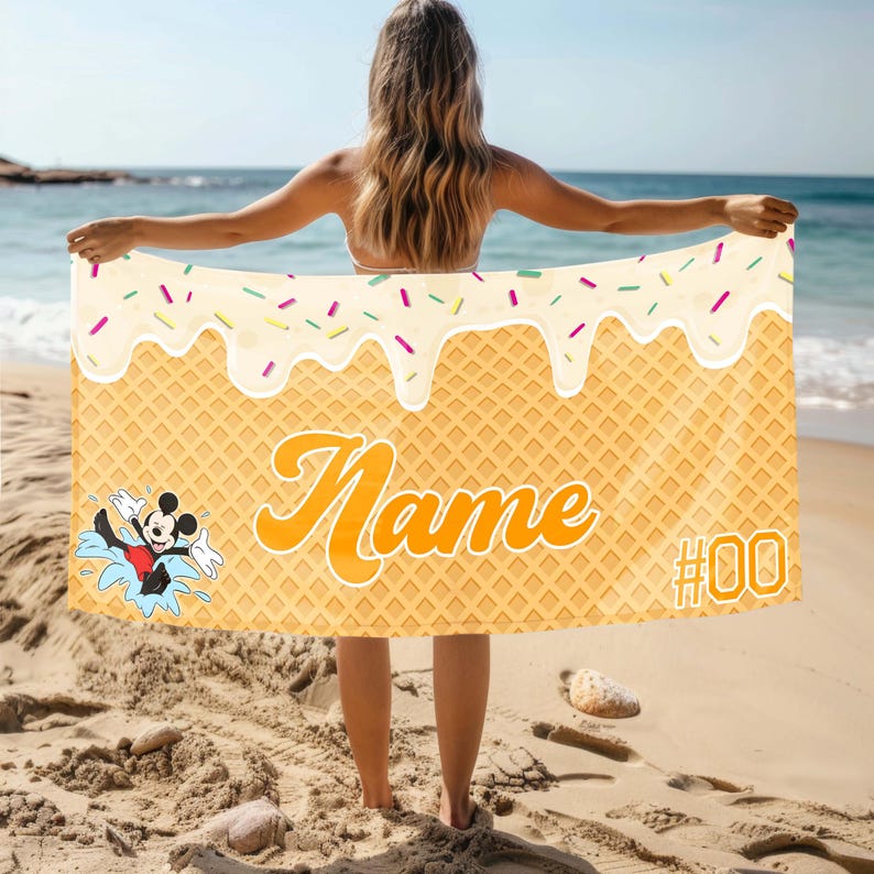 May include: A yellow and white beach towel with a waffle pattern and a white icing design. The towel has a cartoon image of Mickey Mouse swimming and the text "Name #00".