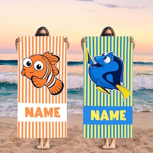 May include: Two beach towels with colorful striped patterns. One towel features a cartoon image of Dory the blue tang fish with the text "NAME". The other towel features a cartoon image of Nemo the clownfish with the text "NAME".