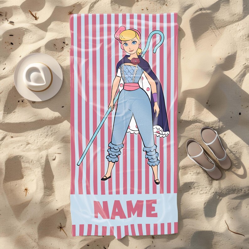 May include: A pink and white striped beach towel with a cartoon image of a female character holding a staff. The character is wearing a blue dress and a pink hat. The text "NAME" is printed on the towel.