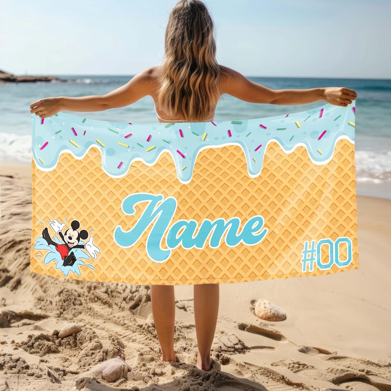 May include: A blue and yellow beach towel with a waffle pattern and a blue ice cream drip design. The towel features a cartoon Mickey Mouse character and the text "Name #00".