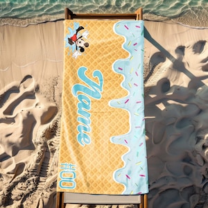 May include: A yellow and blue beach towel with a waffle pattern and a blue ice cream drip design. Mickey Mouse is jumping out of the ice cream. The towel says "Name" and "#000".