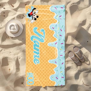 May include: A yellow and blue beach towel with a waffle pattern. The towel has a blue ice cream drip with sprinkles and the text "Name #000". A cartoon image of Mickey Mouse is in the top left corner.