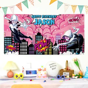 May include: A pink banner with the text "HAPPY BIRTHDAY JASON" and illustrations of a superheroine. The banner also features cityscape silhouettes and comic book style sound effects like "BANG" and "POW!"
