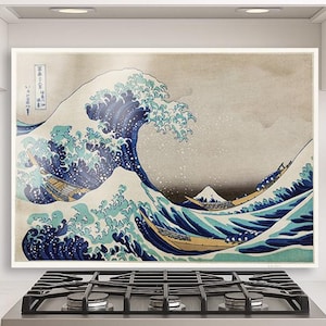 Puede incluir: Impresión enmarcada de "La gran ola de Kanagawa" de Hokusai. La obra representa una gran ola oceánica con barcos y el monte Fuji al fondo. La impresión presenta tonos de azul, blanco y beige, con texto japonés.
