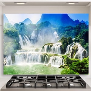 Puede incluir: Una imagen vibrante de una cascada en cascada con múltiples niveles, rodeada de exuberante follaje verde e imponentes montañas azules. El agua fluye hacia una piscina turquesa, creando una escena de paisaje natural serena.