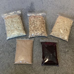 May include: Five clear plastic bags containing different types of wood shavings. The bags are arranged in a row on a grey surface.
