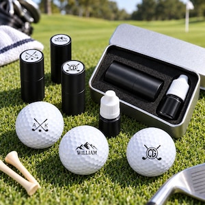 Puede incluir: Un set de accesorios de golf que incluye tres pelotas de golf blancas con diseños negros, tres marcadores cilíndricos negros con logotipos a juego, dos frascos negros pequeños con tapas blancas, una caja de metal y dos tees de madera.