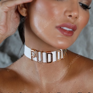 May include: White leather choker with gold-colored letters spelling "PUDDIN".
